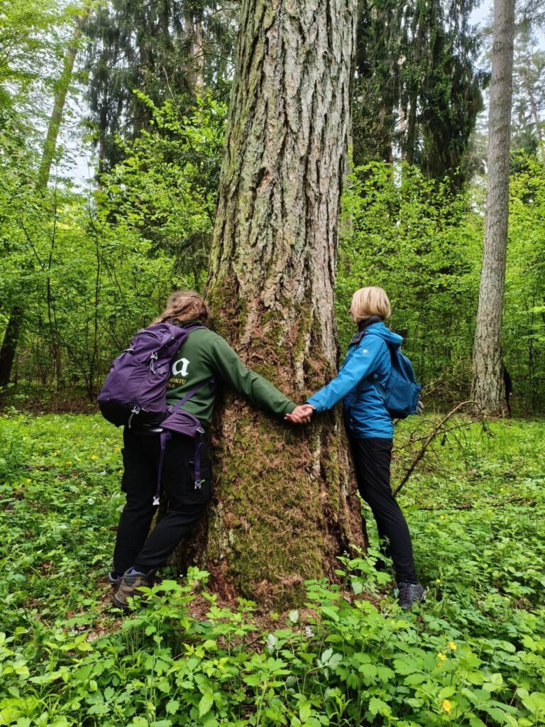 Žaliosios gamtos mokyklos bendruomenės nariai prisiliečia prie medžio ir patiria ryšį su gamta